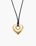 Amara Necklace, polished gold-tone puffed heart pendant with open center on black waxed cord, on white