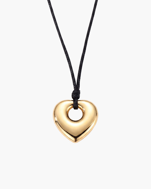 Collar Amara, colgante pulido de corazón abombado en tono dorado con el centro abierto en cordón negro encerado, sobre fondo blanco